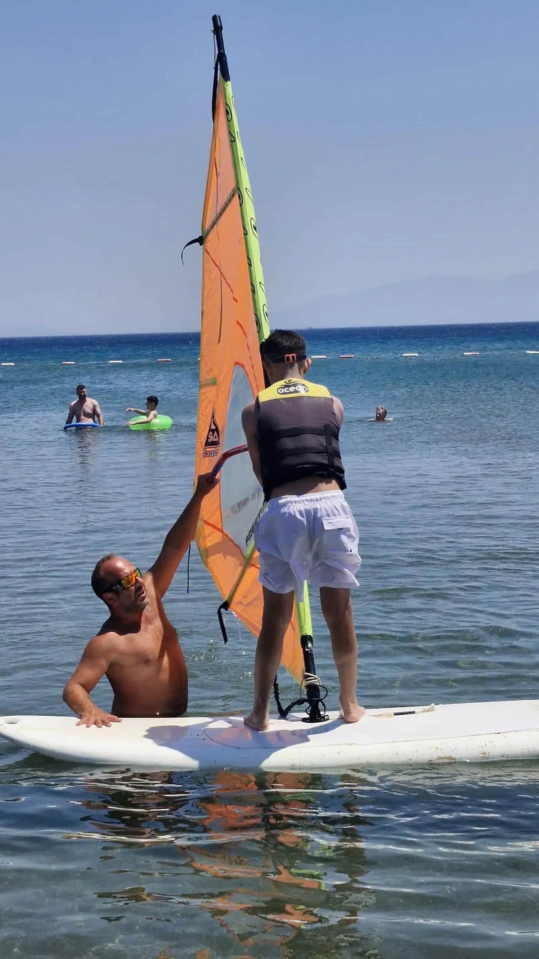 An instructor demonstrating sail control to a participant on the board at Vela