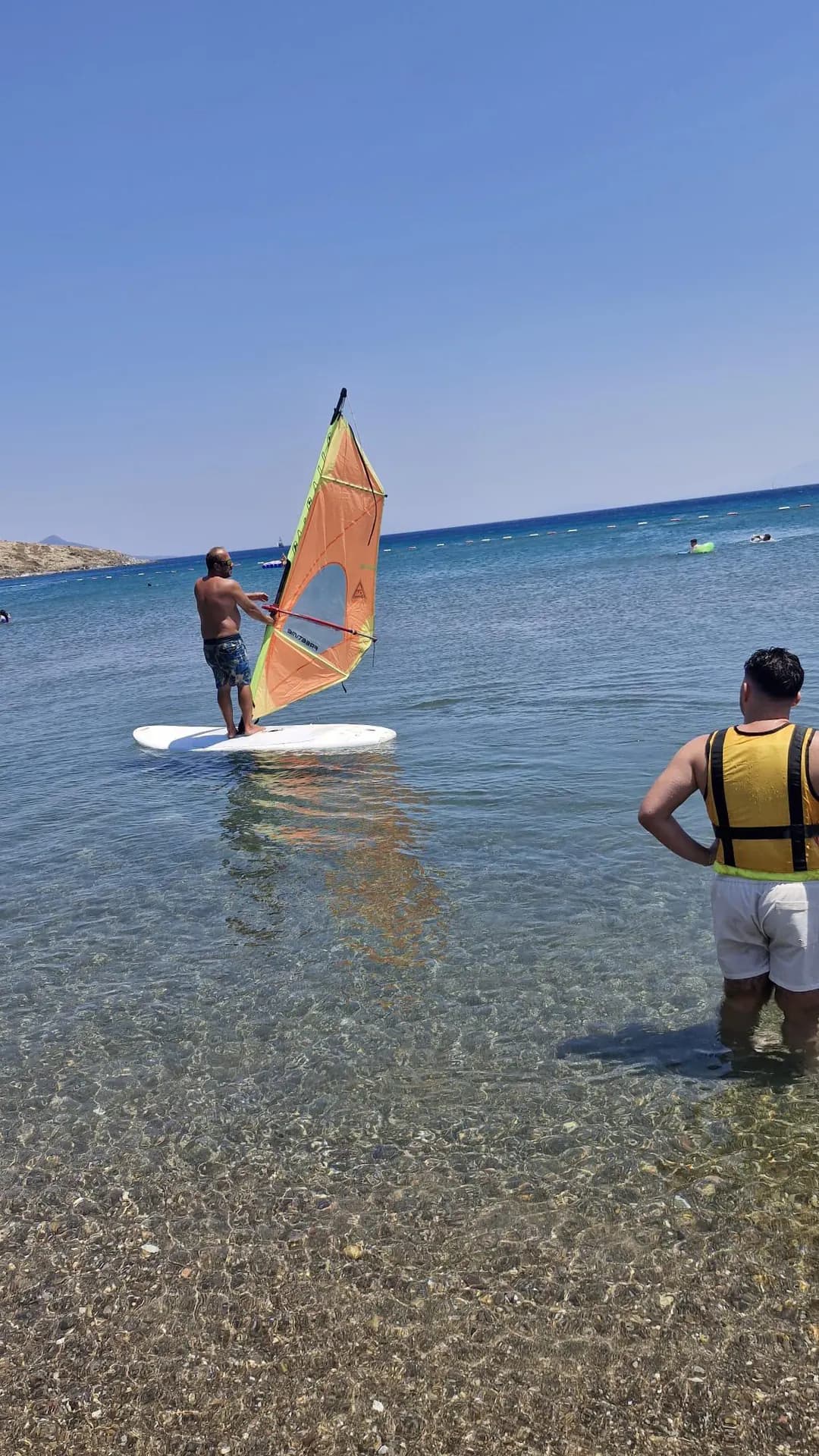 Windsurf participant balancing with an orange sail in shallow water